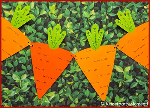 Girlande aus dreieckigen orangen Papierstücken mit grünen Karottengrün-Formen und dem wiederholten Schriftzug 'HAPPY PARTY' vor grünem Blatt-Hintergrund