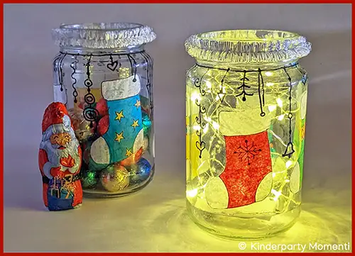Zwei mit Weihnachtsmotiven verzierte Gläser, eines mit Lichterkette beleuchtet, daneben eine Schokoladenfigur in Weihnachtsmannform