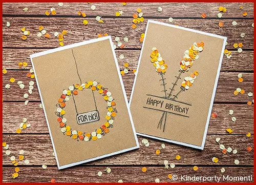 Zwei handgemachte Grußkarten mit Blumenblätter-Konfetti auf Holztisch, eine mit Kranz und Schild 'FÜR DICH', die andere mit Blumenstrauß und Schriftzug 'HAPPY BIRTHDAY'