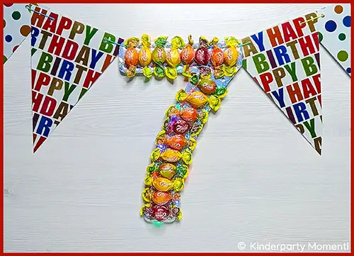 Geburtstagsgirlande mit bunten Buchstaben und eine große Zahl 7 aus bunten Bonbons mit kleinen Lichtern