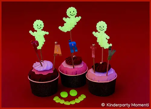 Drei Cupcakes mit bunten Buchstaben und leuchtenden Figuren aus Bügelperlen als Cake Topper vor rotem Hintergrund