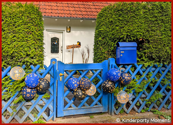 Luftballon Deko für Kindergeburtstag an blauen Holzzaun hängen blaue Luftballons mit goldenen Sternen, im Hintergrund ein Haus