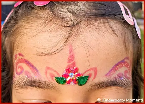 Stirn mit glitzerndem Einhorn-Make-up und einer kleinen Blume mit grünen Blättern in der Mitte