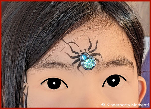 Kindergesicht mit aufgeklebter Glitzer Spinne auf der Stirn.