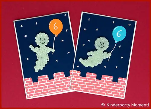 Zwei Karten mit Gespenstern aus Bügelperlen, die jeweils einen Luftballon mit der Zahl 6 halten, vor einem Nachthimmel mit Sternen und einer roten Ziegelmauer