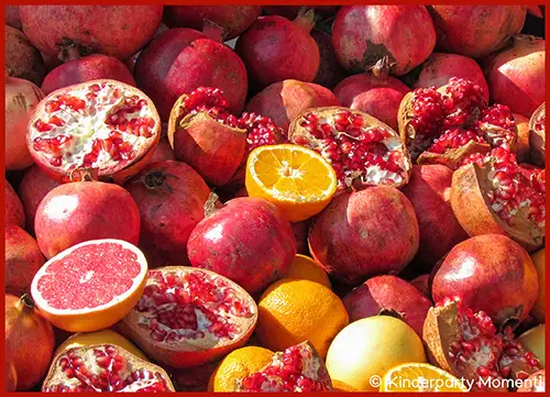 Mehrere ganze und aufgeschnittene Granatäpfel sowie eine aufgeschnittene Orange und eine ganze Orange liegen dicht beieinander
