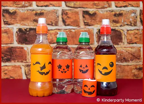 Fünf Flaschen mit Halloween-Etiketten, die lachende Halloween Kürbisgesichter zeigen, vor Ziegelsteinwand