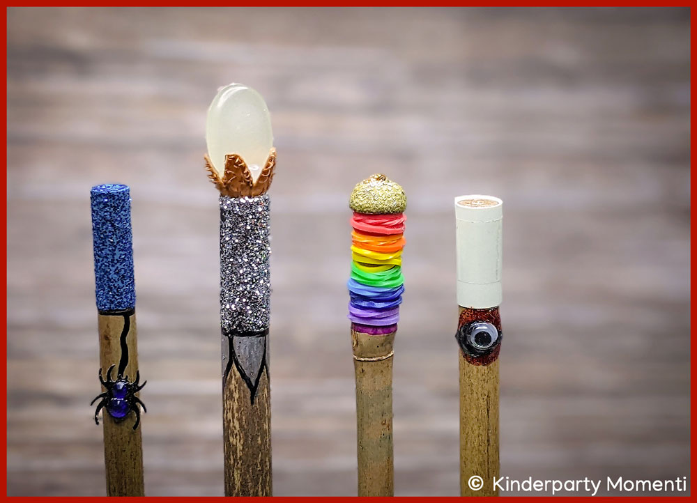 Vier bunte DIY Zauberstäbe mit verschiedenen Verzierungen vor einem Holzhintergrund