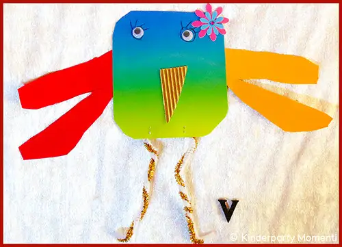 Buntes, quadratisches Papier mit aufgeklebten Wackelaugen, einer gelben Papierspitze als Schnabel, roten und gelben Papierstreifen als Flügel und gedrehten Schnüren als Beine auf weißem Hintergrund