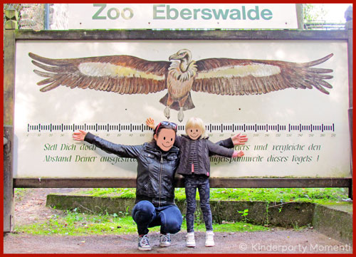 Mutter und Kind mit ausgestreckten Armen vor einem Bild eines Vogels im Zoo Eberswalde