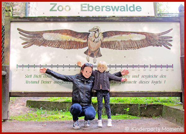 Mutter und Kind mit ausgestreckten Armen vor einem Bild eines Vogels im Zoo Eberswalde