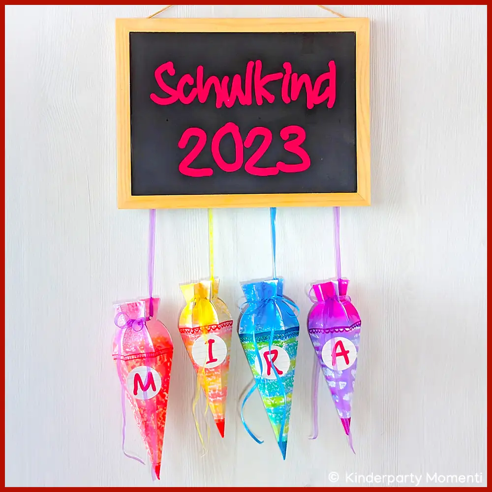 Einschulungsdeko aus Tafel und kleinen Schultüten Auf einer kleinen Tafel steht Schulkind 2023. An der Tafel hänge vier bunte, selbstgebastelte, kleine Schultüten.