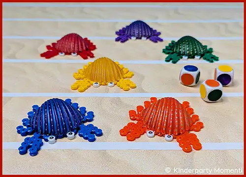 Sechs bunte Krabbenfiguren aus Perlen mit Augen auf einem Spielfeld neben zwei Würfeln mit farbigen Punkten