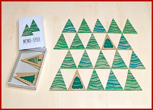 Dreieckige Memo-Spielkarten mit grünen Tannenbaum-Motiven und einer passenden Spielschachtel auf hellem Untergrund