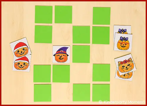 Mehrere grüne Memo Spielkarten liegen verdeckt auf einem hellen Holztisch, einige Karten zeigen fröhlichen Halloween Kürbis-Motive
