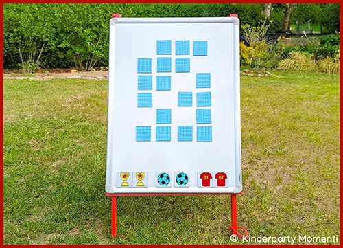 Magnettafel mit verdeckten quadratischen Karten und Magneten in Form von Pokalen, Fußbällen und Trikots auf einer Wiese