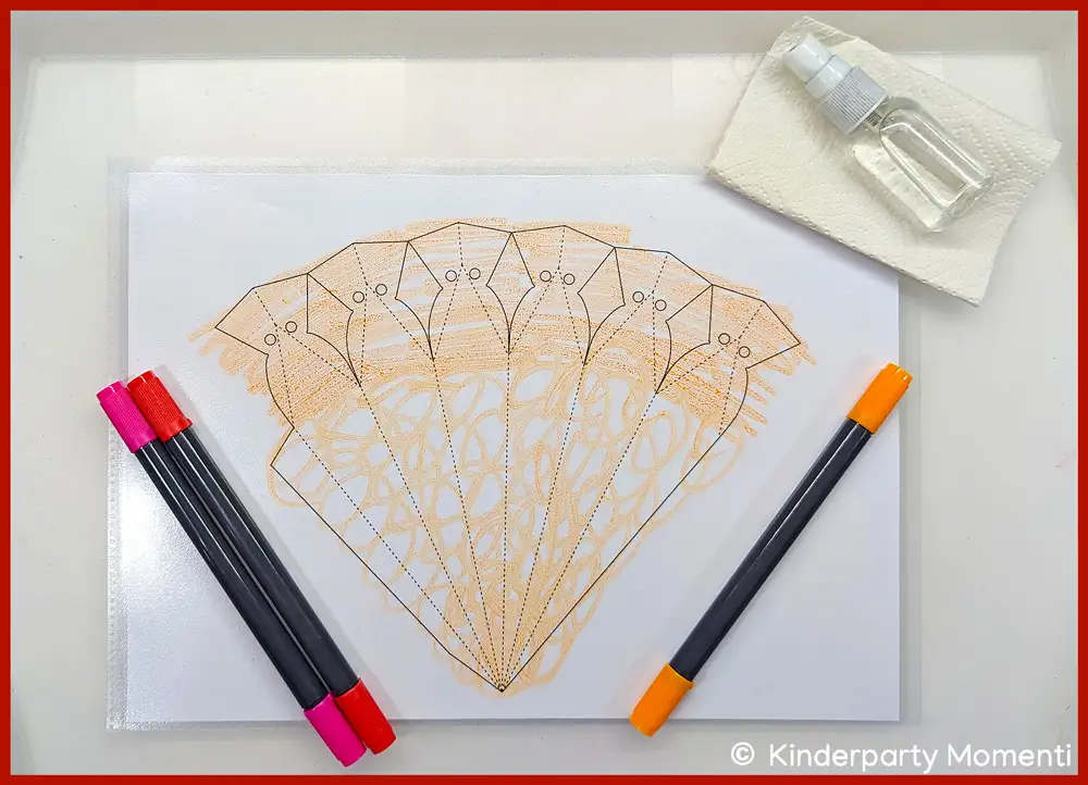 Prospekthüllen-Folie in Form der Schultüte bemalen Prospekthüllen-Folie in Schultüten Form bemalt mit orangem Stift auf einem Tablett.