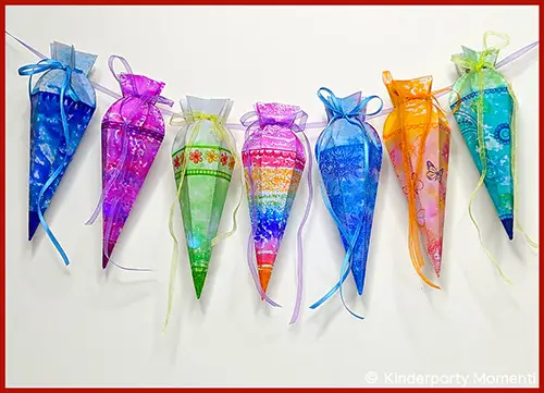 Sieben bunte Mini-Schultüten aus Papier mit verschiedenen Mustern und Schleifen hängen an einer Schnur