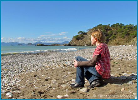 Frau sitzt an Strand und schaut aufs Meer