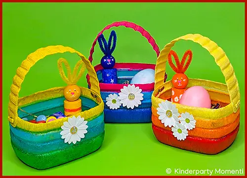 Drei bunte Osterkörbchen mit Hasenfiguren und künstlichen Blumen vor grünem Hintergrund