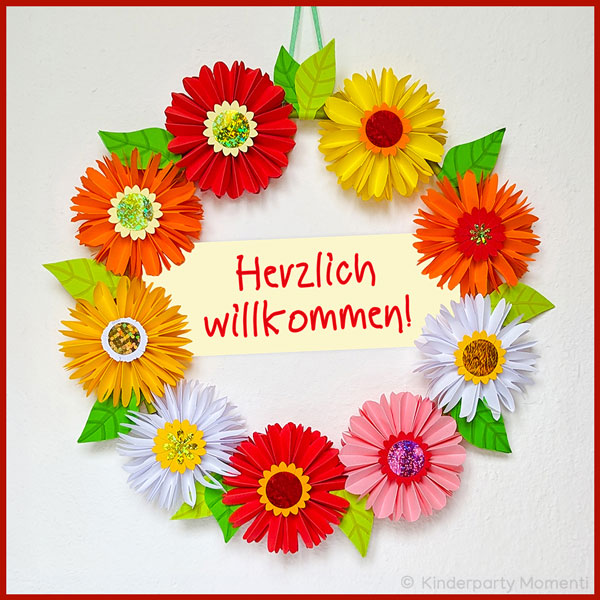 Dekokranz aus fröhlich bunte Papierblumen mit Herzlich willkommen Schild bunte aus Papier gefaltete Blumen bilden eine Kranz in deren Mitte Herzlich willkommen steht