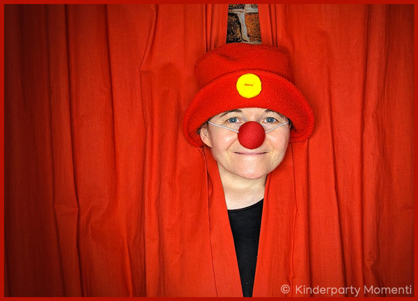 Frau mit roter Clownsnase schaut durch einen Vorhang