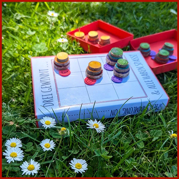 Kleines Spiel zum Mitnehmen in den Park ein Tic-Tac-Toe-Spiel mit Schnecken Spielsteinen liegt auf einer Wiese
