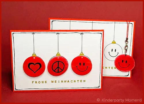 Weihnachtskarte mit drei roten Kugeln, darauf ein Herz, ein Peace-Zeichen und ein Smiley, darunter der Schriftzug 'FROHE WEIHNACHTEN'