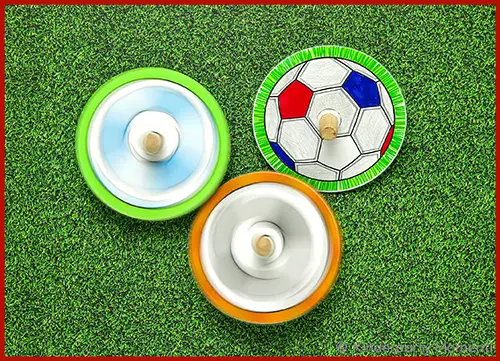 Drei selbstgebastelte Kreisel auf grünem Rasen, einer mit Fußballmuster und zwei in Bewegung mit grünem und orangefarbenem Rand