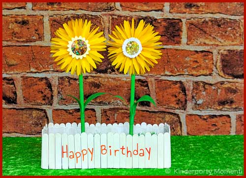 zwei Papierblumen stehen in einem kleinen Blumenkasten mit der Aufschrift Happy Birthday
