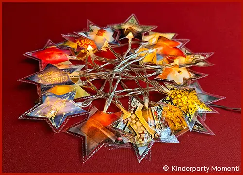 Sternförmige Lichterkette mit bunten, gemusterten Papiersternen auf rotem Untergrund