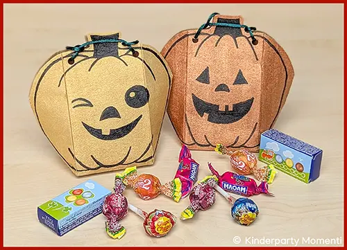 Zwei Kürbis Halloween Taschen mit aufgemalten lachenden Gesichtern, davor verschiedene bunte Süßigkeiten.