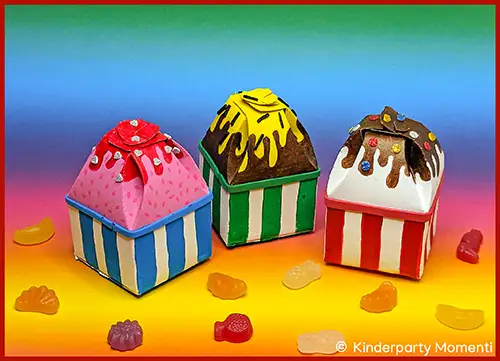 Drei kleine Tetrapak-Kartons mit gestreiftem Muster und Deckeln, die wie Eistüten mit Zuckerguss und Streuseln aussehen, umgeben von Gummibärchen.