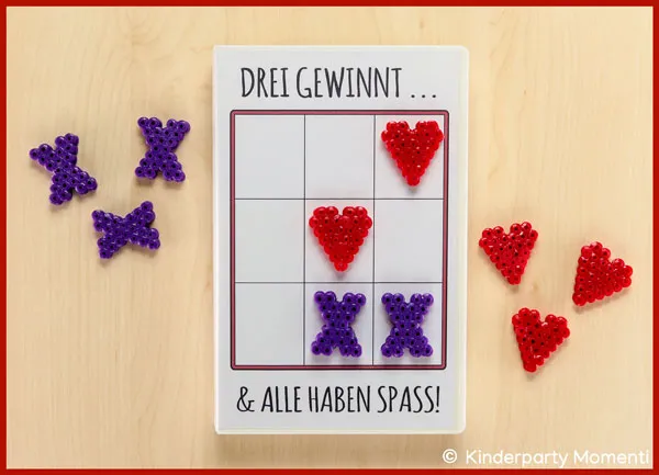 Tic-Tac-Toe Spiel mit Spielsteinen aus Bügelperlen auf einem Tisch liegt ein Tic-Tac-Toe Spiel in einer VHS Hülle mit Spielfiguren aus Bügelperlen