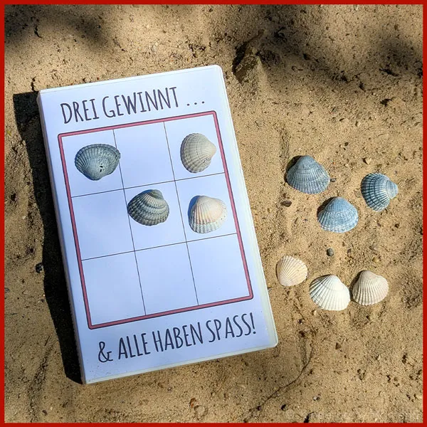 Reisespiel mit Muscheln ein Tic-Tac-Toe-Spiel mit Muscheln liegt am Strand im Sand