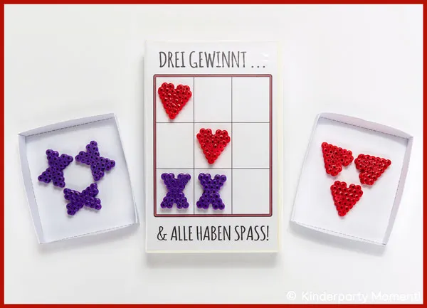 auf einem Tisch liegt ein Tic-Tac-Toe Spiel in einer VHS-Hülle mit Bügelperlen-Motiven als Spielfiguren