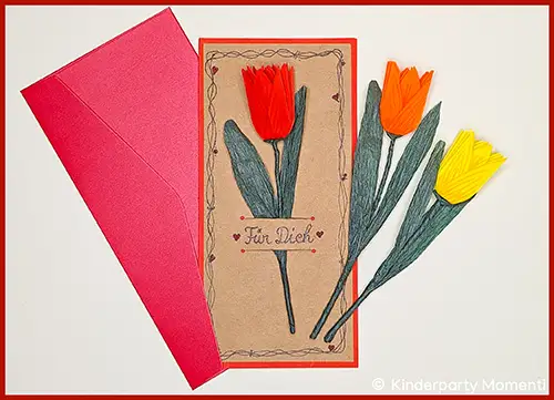 Drei gefaltete Tulpen aus Papier in Rot, Orange und Gelb mit grünen Blättern neben einer Karte mit der Aufschrift 'Für Dich' und einem roten Umschlag