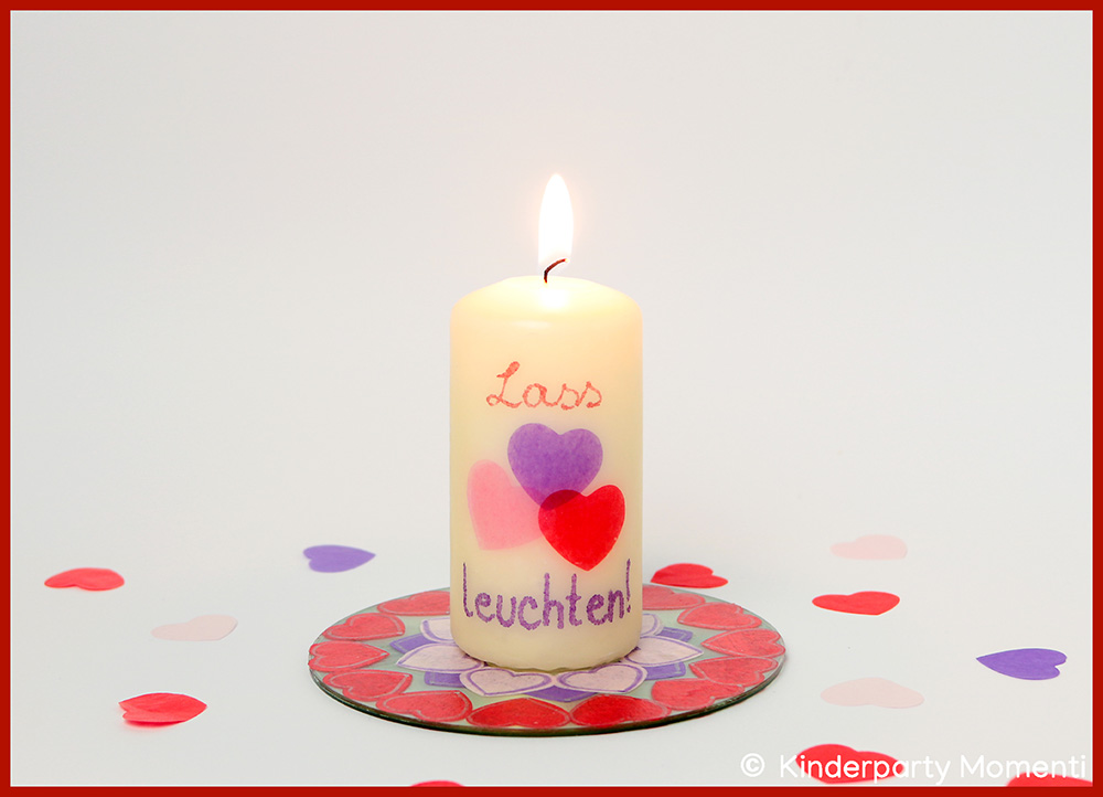 Brennende Kerze mit dem Spruch 'Lass Herzen leuchten' und mehreren Herzmotiven auf einem runden Untersetzer mit Herzmuster