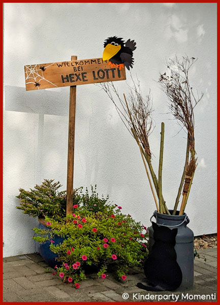 Willkommensschild mit kleinem Raben Holzschild mit kleinem Raben, Aufschrift Willkommen bei Hexe Lotti, daneben eine Milchkanne mit Hexenbesen