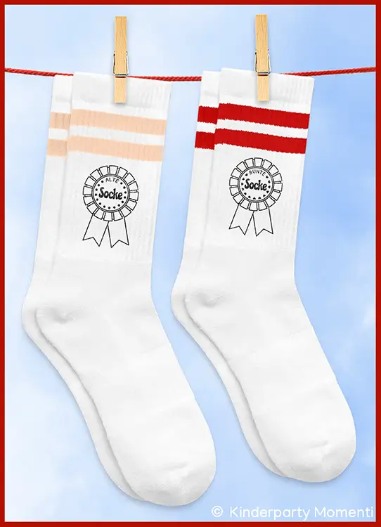Zwei weiße Socken mit je zwei farbigen Streifen oben, links in Pastellorange, rechts in Rot, beide mit einem Aufdruck eines Ordens mit dem Wort 'Alte Socke' und 'Bunte Socke' in der Mitte, an einer roten Leine mit Holzklammern aufgehängt