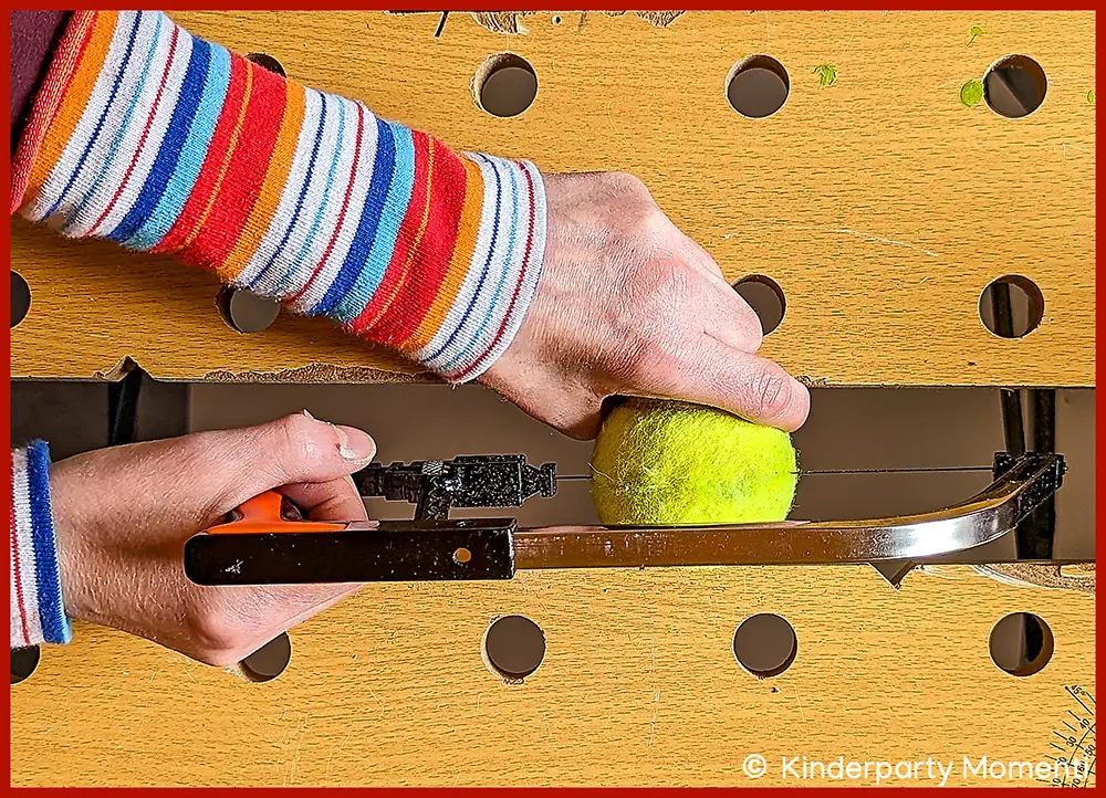 Werkbank, auf der Hände mit einer Säge einen Tennisball aufsägen.