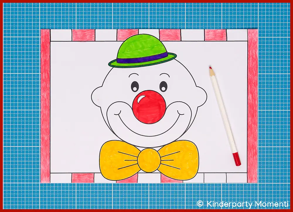 Ausgemalte Vorlage eines Clownsgesichts mit grünem Hut, roter Nase und gelber Fliege auf Bastelmatte, daneben ein roter Buntstift
