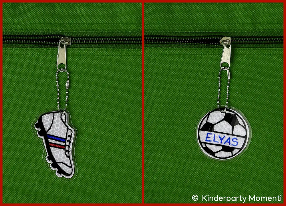 DIY Reflektor Anhänger - Fußballschuhe & Fußball Zwei reflektierende Anhänger an grüner Stofftasche, einer in Form eines Fußballschuhs mit blauen und roten Streifen, der andere rund mit einem Fußballmuster und dem Namen 'ELYAS'
