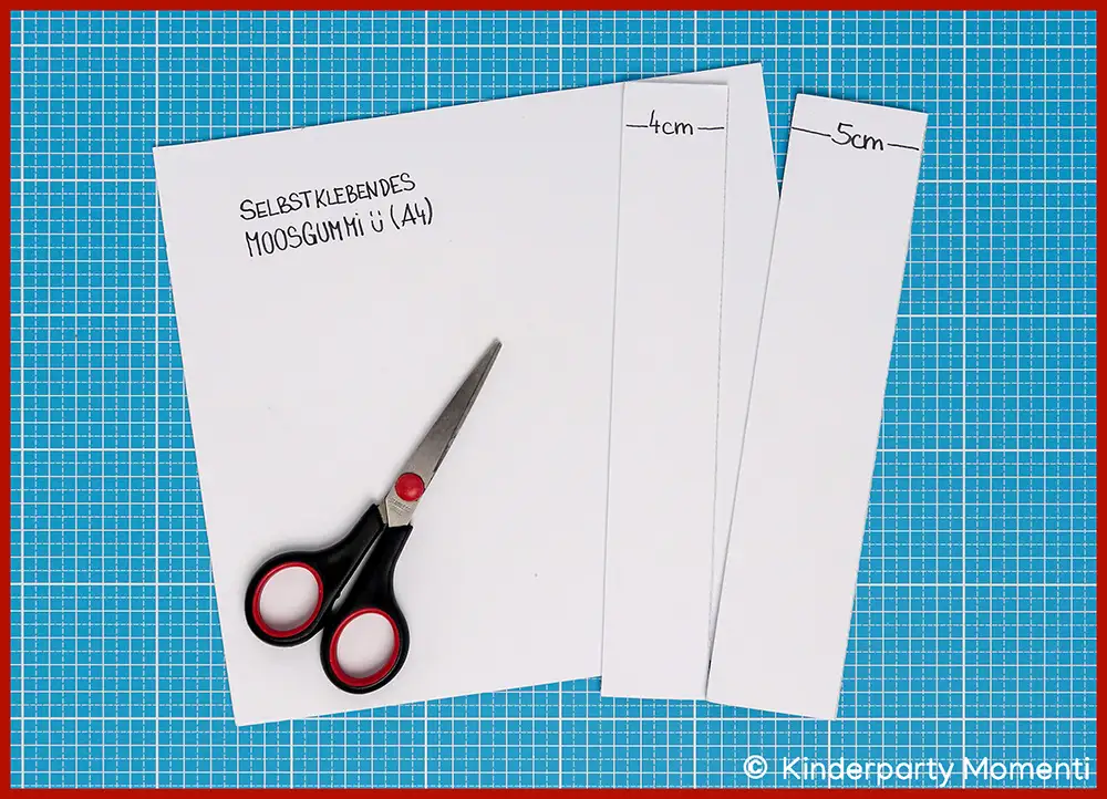 Schere liegt auf zugeschnittenen weißen Moosgummibögen mit handschriftlichen Maßen und Text auf blauem Schneideunterlage