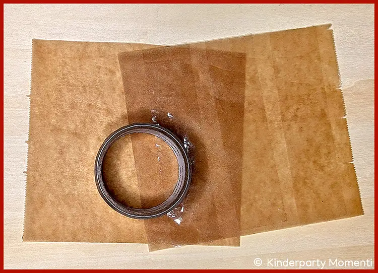 Breites, transparentes Klebeband auf Backpapier kleben Rolle transparentes Klebeband auf mehreren überlappenden braunen Backpapierstücken auf hellem Untergrund