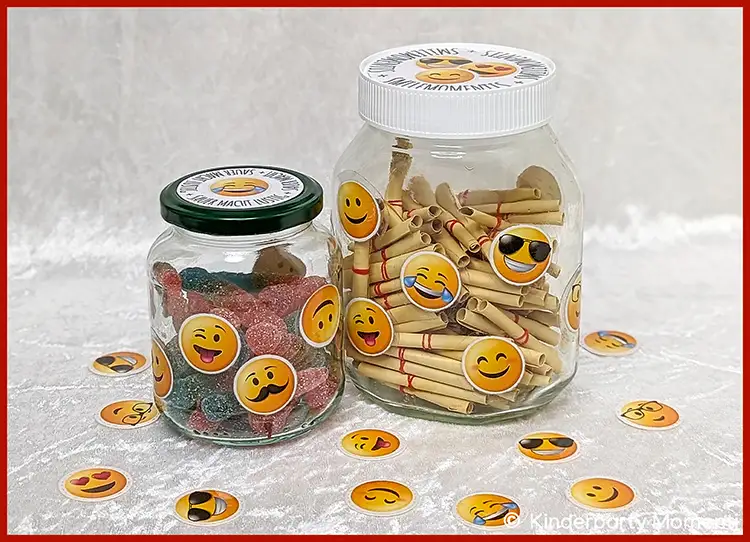 Zwei Gläser mit bunten Süßigkeiten und gerollten Zetteln, beklebt mit verschiedenen Emoji-Stickern, umgeben von verstreuten Emoji-Stickern auf grauem Untergrund