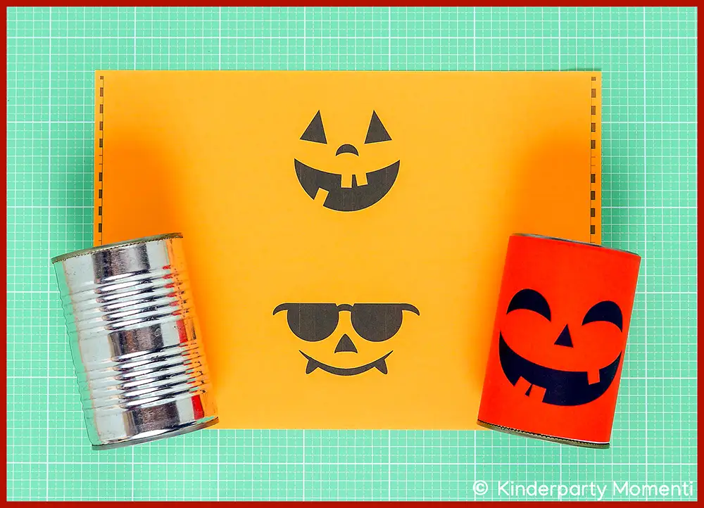 Dosenwerfen zum Selbermachen mit Halloween Kürbisgesichter Vorlagen zum Ausdrucken Zwei Blechdosen, eine silberne und eine beklebt mit rotem Papier mit Halloween Gesicht, beide liegen auf einer orangefarbenen Papier Vorlage mit zwei weiteren Halloween-Gesichtern.