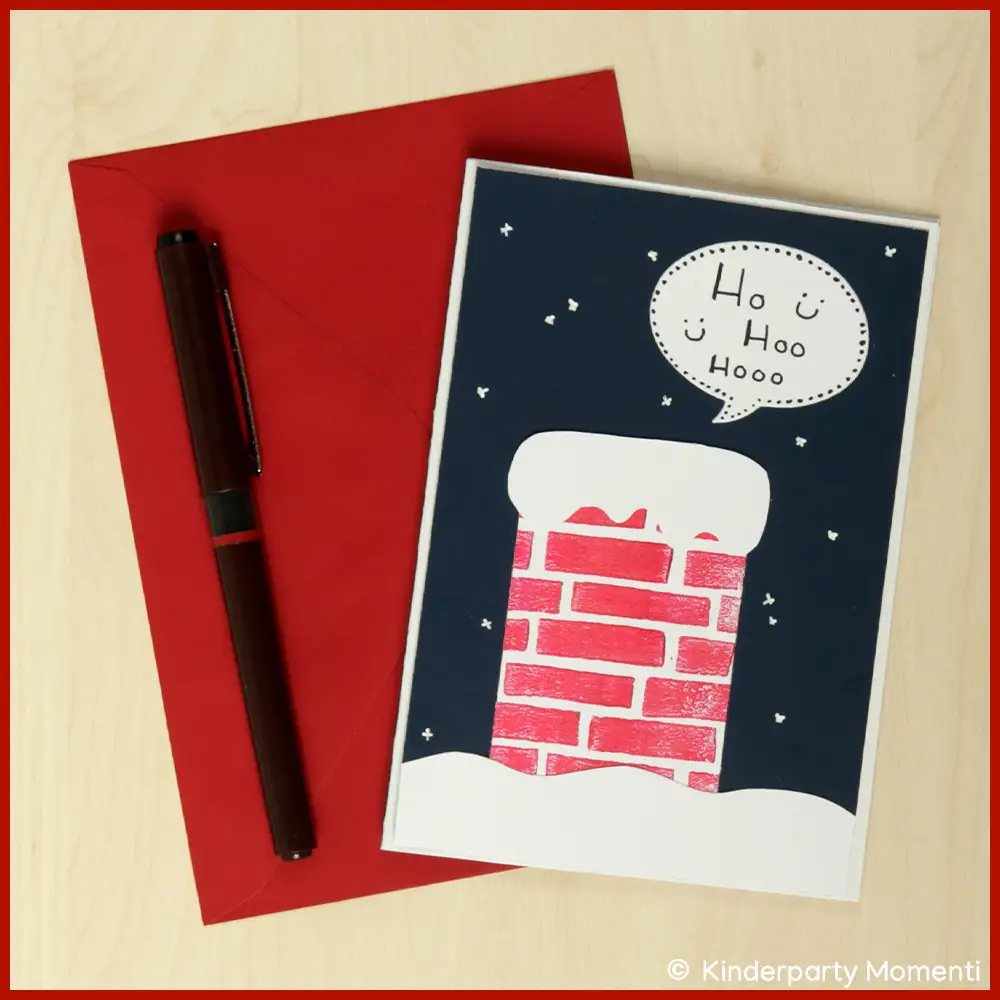 Selbstgebastelte Weihnachtskarte mit rotem Briefumschlag und schwarzem Stift, Karte zeigt roten Schornstein mit Schnee und Sprechblase 'Ho Hoo Hooo' vor dunkelblauem Nachthimmel.
