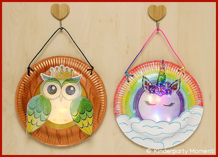 Laternen aus Papptellern mit einer Eule mit Krone und einem Einhorn vor einem Regenbogen und Wolken, beide mit Lichtern im Inneren
