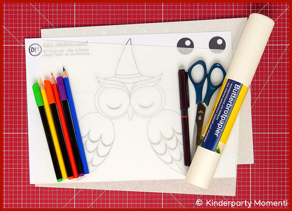 Auf einer roten Bastelmatte liegen Bastelmaterialien für eine Einhornlaterne - Buntstifte, Schere, Filzstifte, Butterbrotpapier und Vorlage mit Eulen Zeichnung.